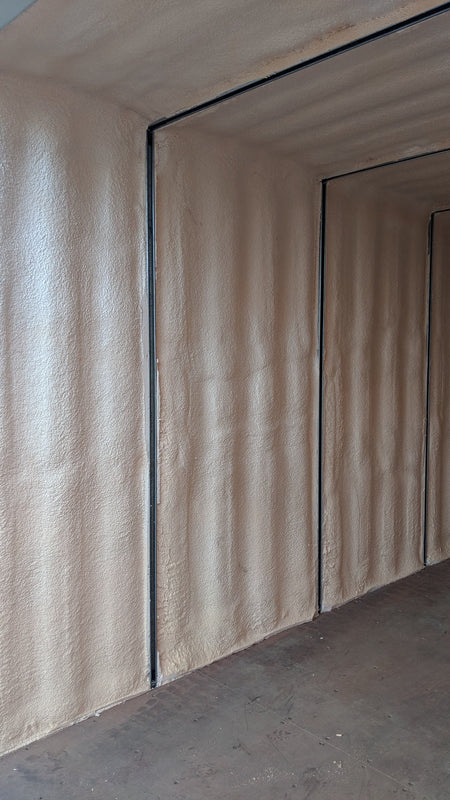 Interior close-up of a spray foam insulated shipping container, showing smooth foam application along corrugated steel walls for enhanced thermal performance and moisture control.