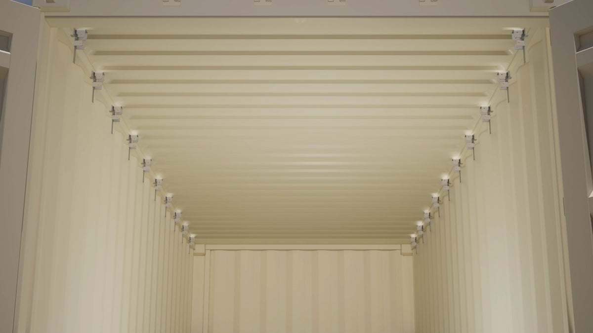 Interior view of a shipping container with aluminum wood stud brackets evenly installed along the top tubing on both walls for framing installation